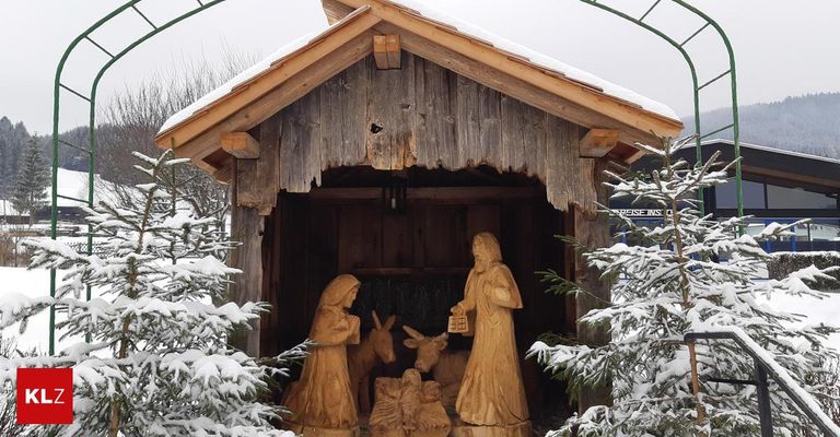 Eine hölzerne Krippe steht draußen im Schnee, mit Statuen von Maria, Josef und Tieren.