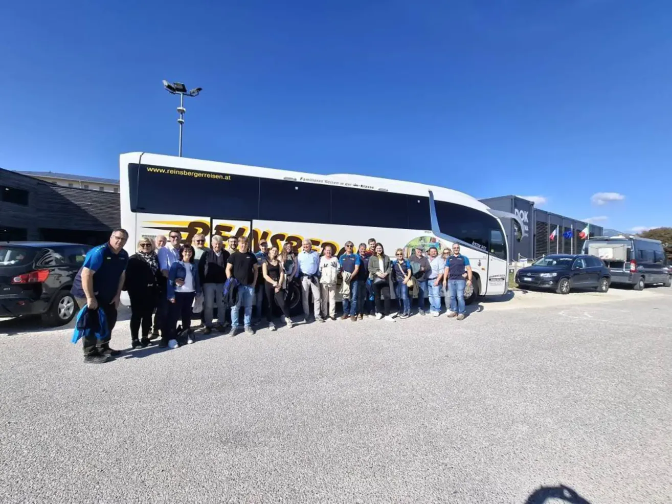 Eine Gruppe von Menschen posiert für ein Foto vor einem weißen Bus, mit einem klaren blauen Himmel im Hintergrund.