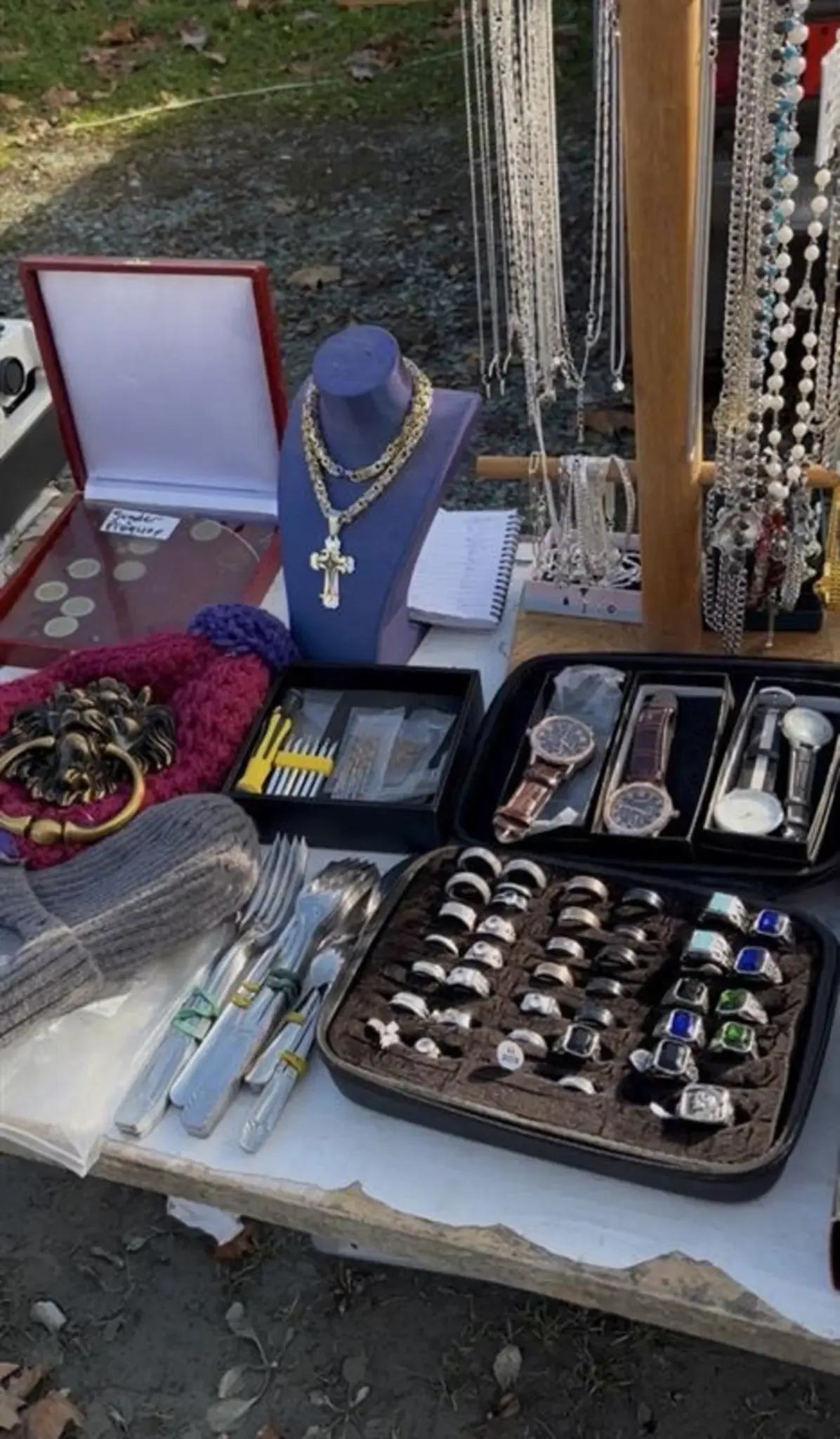 Ein Tisch zeigt eine Auswahl an Artikeln, darunter eine Schachtel mit Münzen, eine Halskette auf einem Mannequin, ein Notizbuch, Ringe in Koffern, einen silbernen Löwen und Silberbesteck.