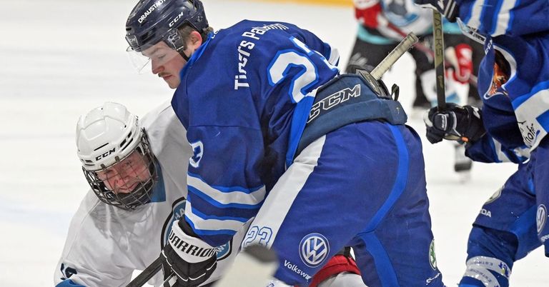 Zwei Eishockeyspieler in blauen Trikots befinden sich auf einer Eisbahn, ein Spieler beugt sich nach vorne, während der andere ihn festhält. Beide tragen Helme und Handschuhe.