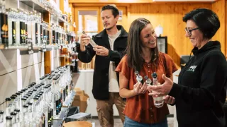 A group of people in a liquor store examining bottles, with a woman smiling and a man holding a bottle.
