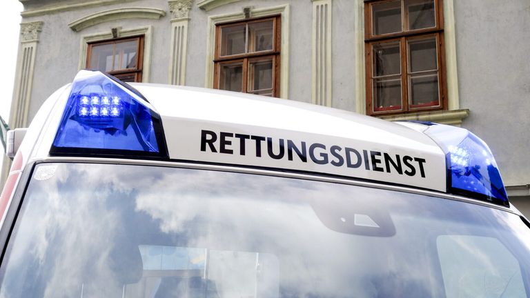 Ein weißer Rettungswagen mit der Aufschrift 'RETTUNGSDIENST' auf dem Dach steht vor einem Gebäude mit drei Fenstern.