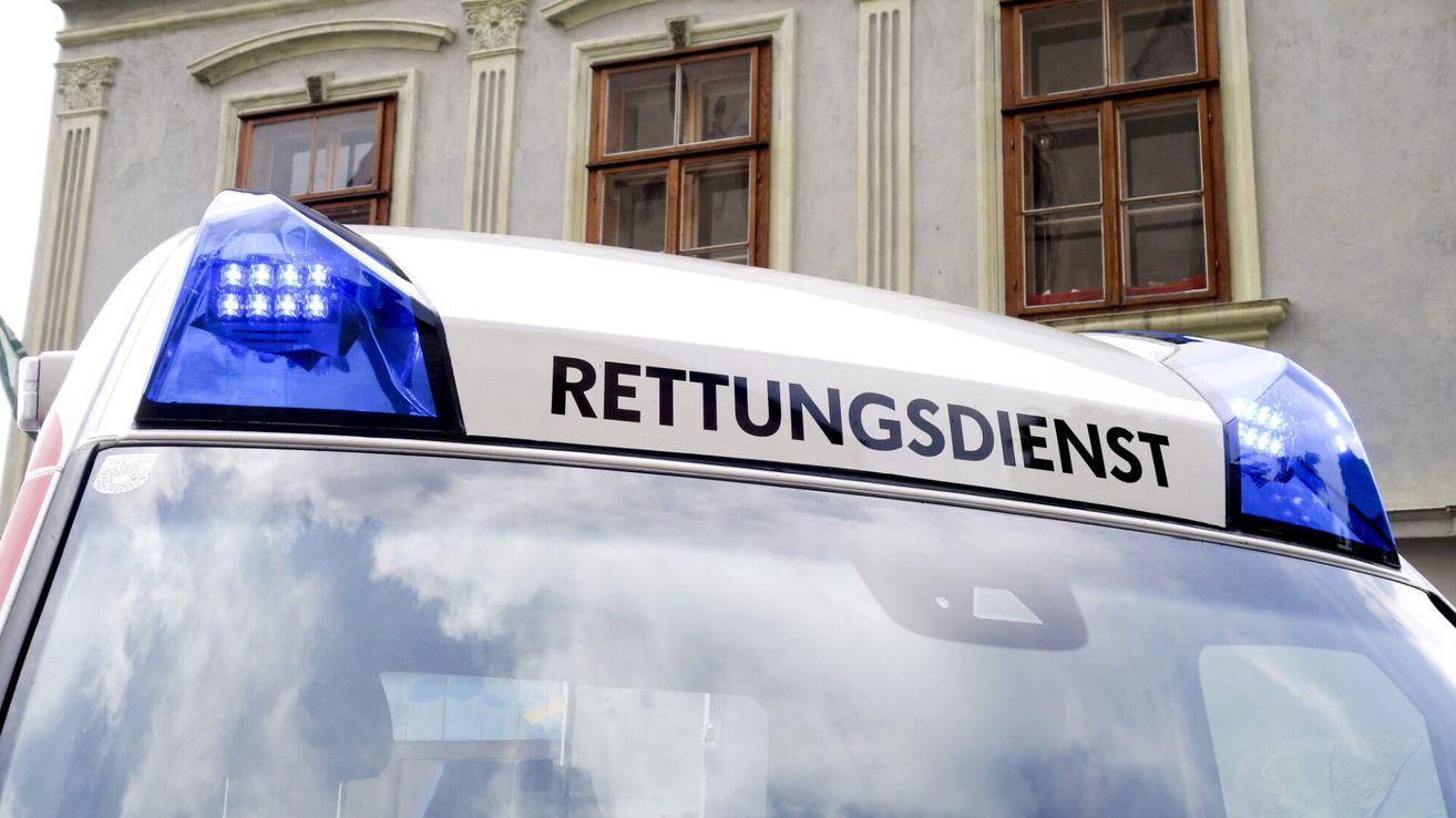 Ein weißer Rettungswagen mit der Aufschrift 'RETTUNGSDIENST' auf dem Dach steht vor einem Gebäude mit drei Fenstern.