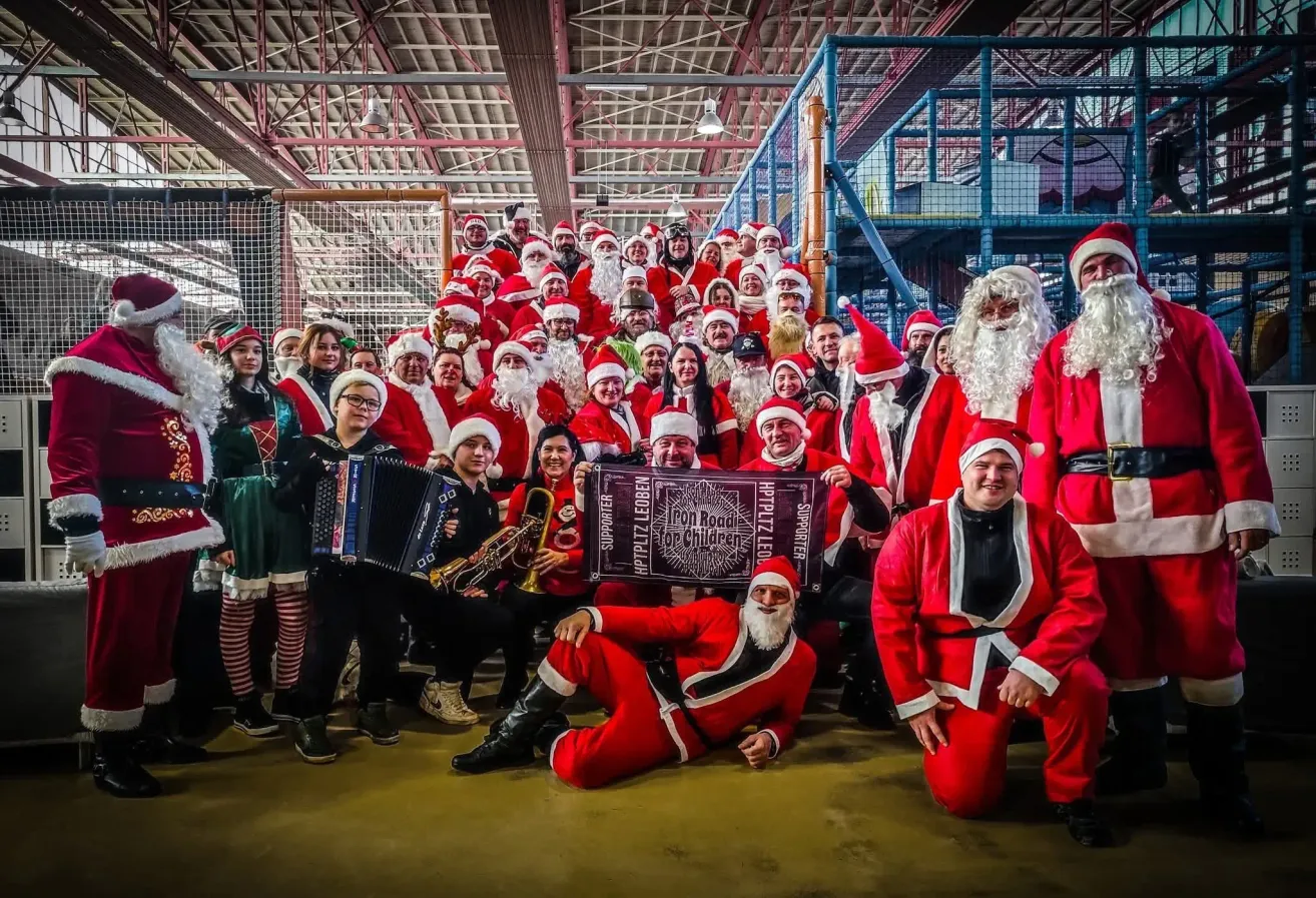 A group of people dressed as Santa Claus posing for a photo with musical instruments, a banner, and an indoor play area in the background.