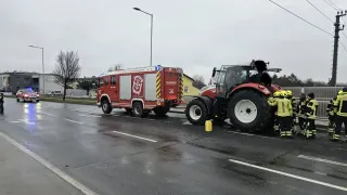 A red fire truck is parked on a wet road next to a tractor. Both vehicles have lights on.