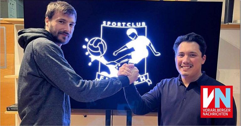 Zwei Männer schütteln sich die Hände vor einem Bildschirm, auf dem das Sportclub-Logo zu sehen ist. Beide lächeln.