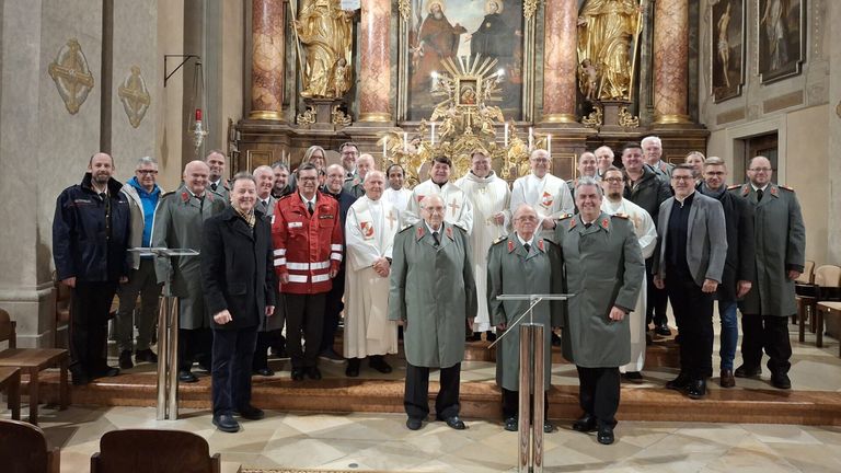 A group of men in uniforms, including firefighters and military personnel, stand in a church with priests, near an altar with candles.