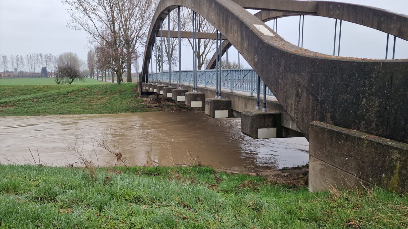 An arch bridge spans a flooded area with muddy water under a gray sky. The concrete bridge has metal railings.