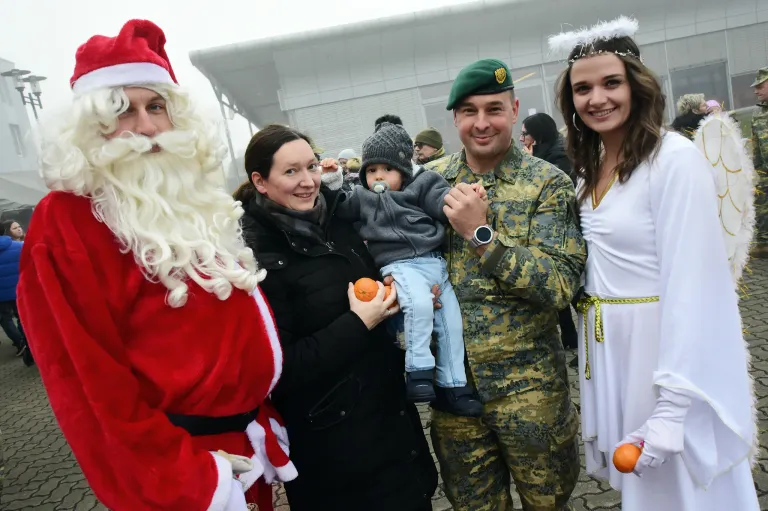 Eine lächelnde Familie und ein Soldat in Uniform posieren für ein Foto mit einem Baby, das eine Orange hält, und dem lächelnden Weihnachtsmann.