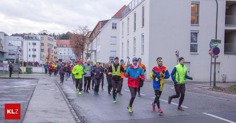 Eine Gruppe von Läufern nimmt an einem Marathon auf einer Stadtstraße teil, mit Zuschauern und Gebäuden im Hintergrund.
