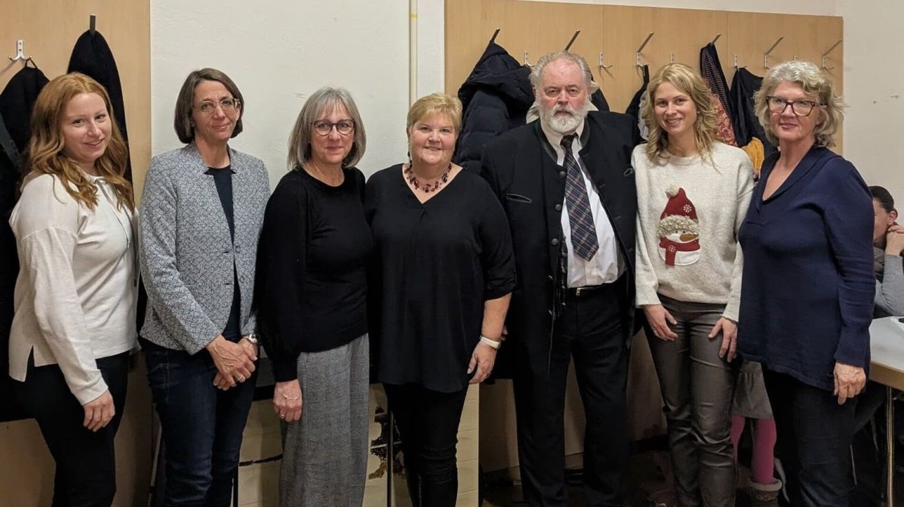 Fünf Personen stehen gemeinsam für ein Foto, möglicherweise bei einer Veranstaltung. Sie tragen Winterkleidung und scheinen zu lächeln.