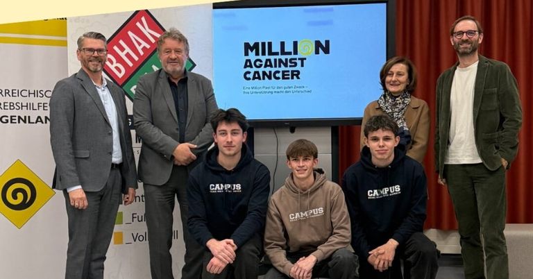 Fünf junge Männer und zwei Erwachsene posieren für ein Foto vor einem Bildschirm mit dem Text 'Million gegen Krebs'.