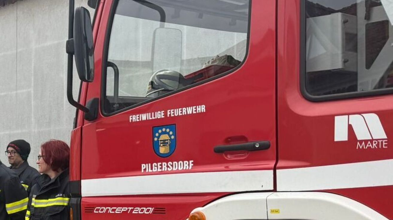 Ein roter Lkw mit weißem Rand hat die Aufschriften 'Freiwillige Feuerwehr' und 'PILGERSDORR'. Der Türgriff ist schwarz. Im Inneren des Lkw befindet sich ein Helm.