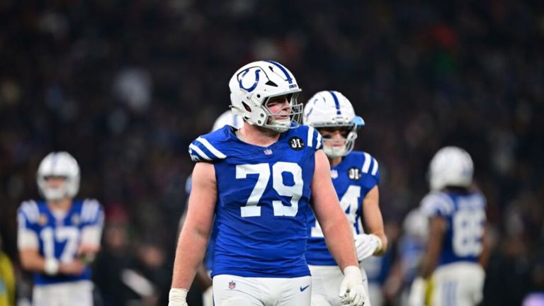 Zwei Footballspieler in blauen Trikots mit den Nummern 79 und 4 stehen auf dem Feld. Einer sieht nach unten, der andere schaut etwas an. Der Hintergrund ist unscharf.