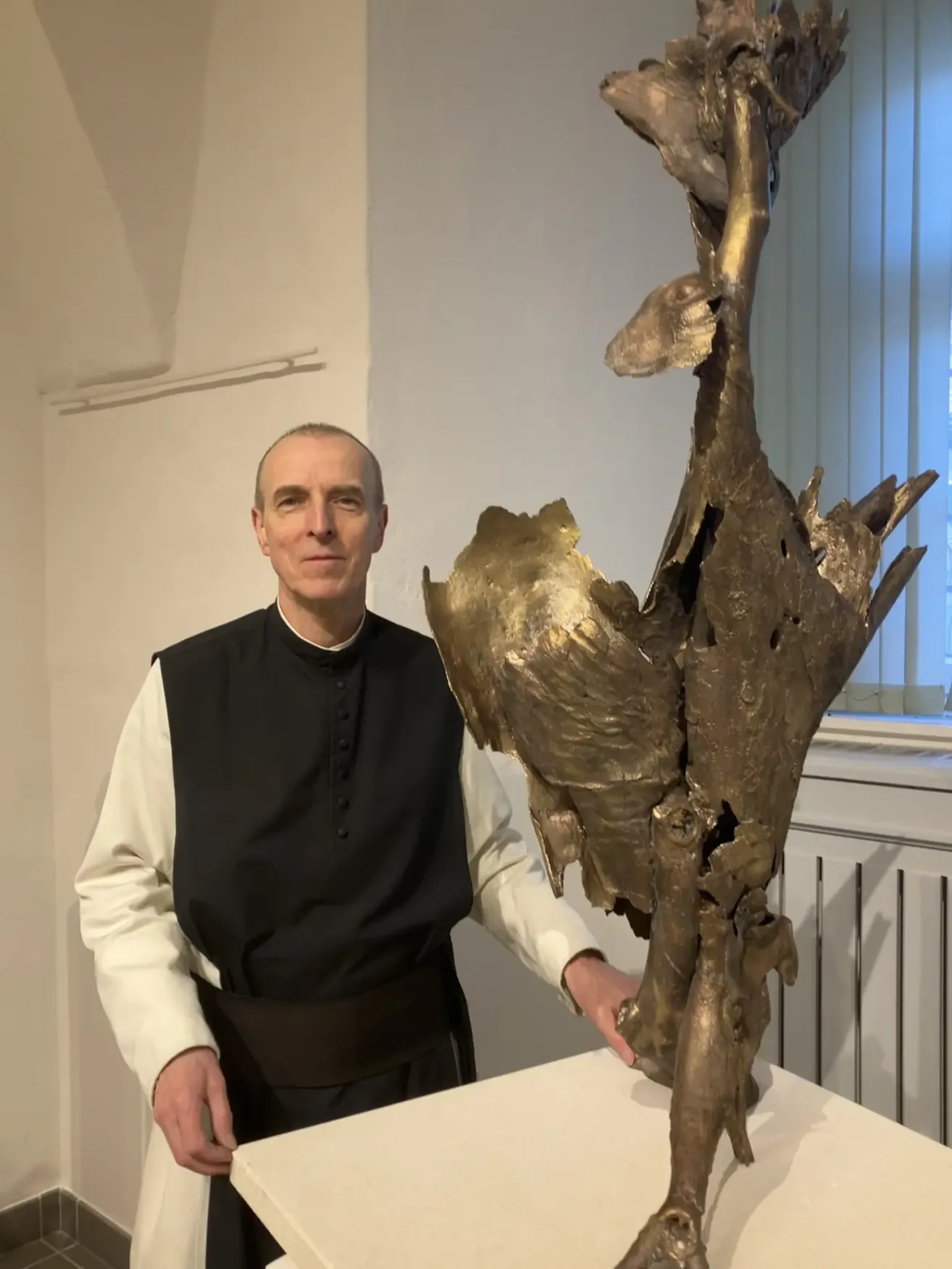 Ein Priester steht neben einer großen goldenen Skulptur mit komplexen, abstrakten Formen, die ihre detaillierte Handwerkskunst und einzigartiges Design hervorhebt.