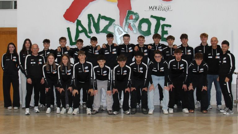 Eine Gruppe von Athleten in gleichen schwarzen und weißen Uniformen posiert für ein Foto vor einer farbenfrohen Wand.