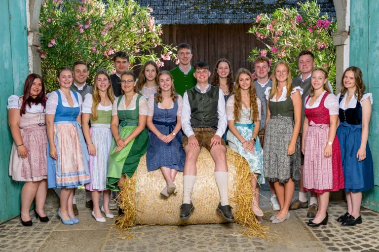 Eine Gruppe junger Menschen in traditioneller Kleidung posiert für ein Foto. Eine Person sitzt auf einem Heuballen.