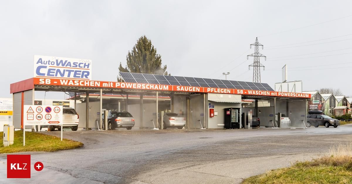 Eine Waschanlage mit Solarpanelen darüber, zwei Autos werden gewaschen, eines ist links geparkt, das andere rechts, mit einem Grasbereich davor.