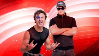 Zwei Männer stehen vor einem roten Hintergrund, einer trägt einen Sicherheitshut und Sonnenbrille, der andere hat Gesichtsbemalung und eine Rock-Geste.