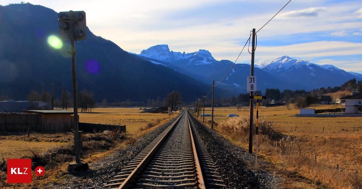 Eisenbahngleise erstrecken sich in die Ferne, eingerahmt von Bergen, mit einem Schild mit der Aufschrift 31 8 und einem Mast in der Nähe.