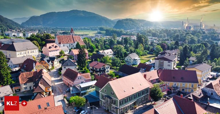 Luftaufnahme einer kleinen Stadt mit bunten Häusern und einer Kirche, umgeben von Bäumen und Bergen, mit einem Sonnenuntergang im Hintergrund.