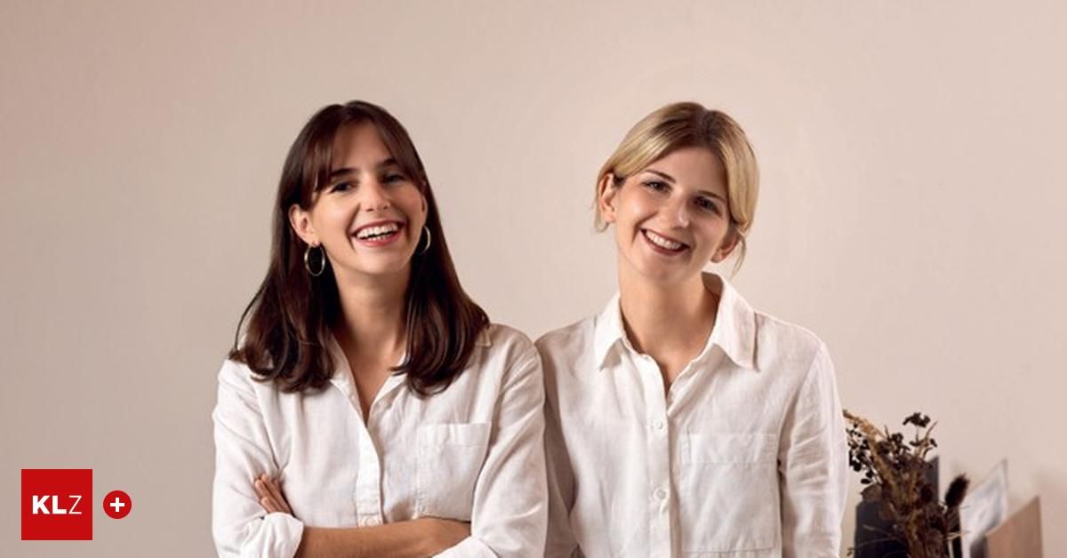 Zwei Frauen lächeln und posieren für ein Foto. Beide tragen weiße Hemden. Die Frau auf der linken Seite hat die Arme verschränkt.