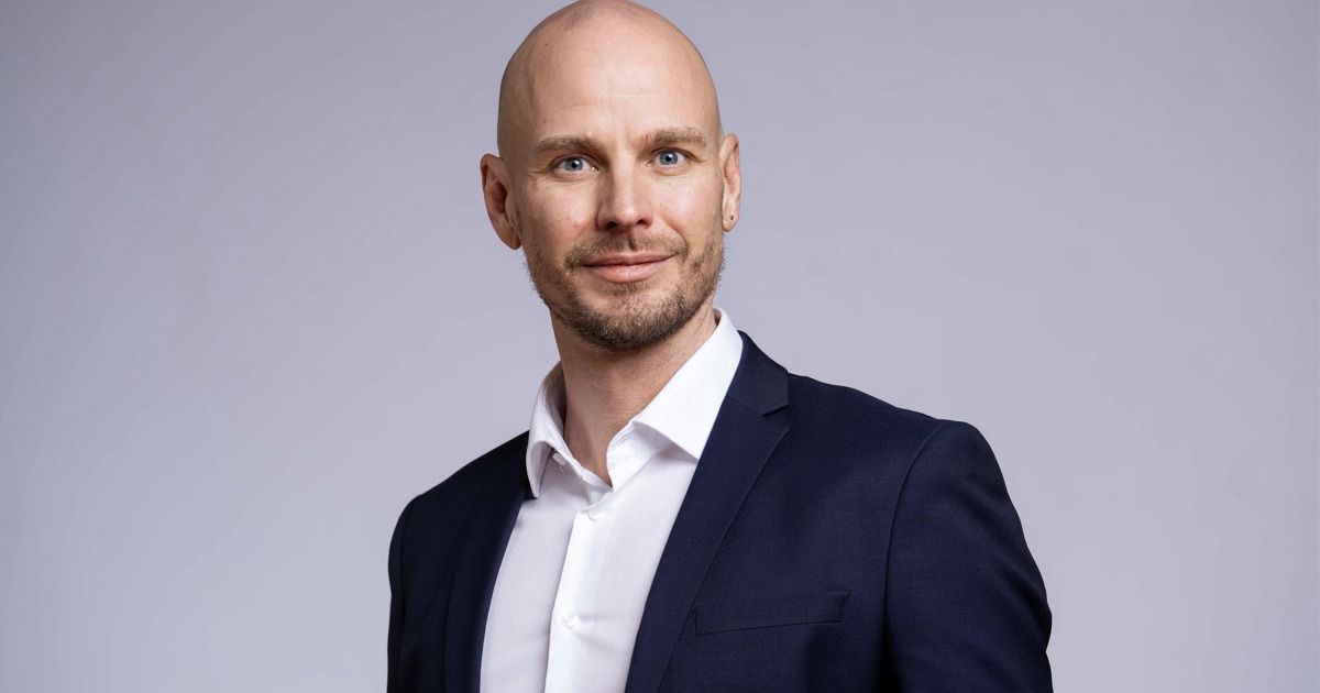 Ein kahlköpfiger Mann mit Bart lächelt in die Kamera. Er trägt einen dunkelblauen Blazer über einem weißen Hemd.