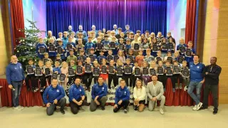 Eine große Gruppe von Kindern und Erwachsenen, die Urkunden halten und für ein Foto posieren. Erwachsene knien vor ihnen.