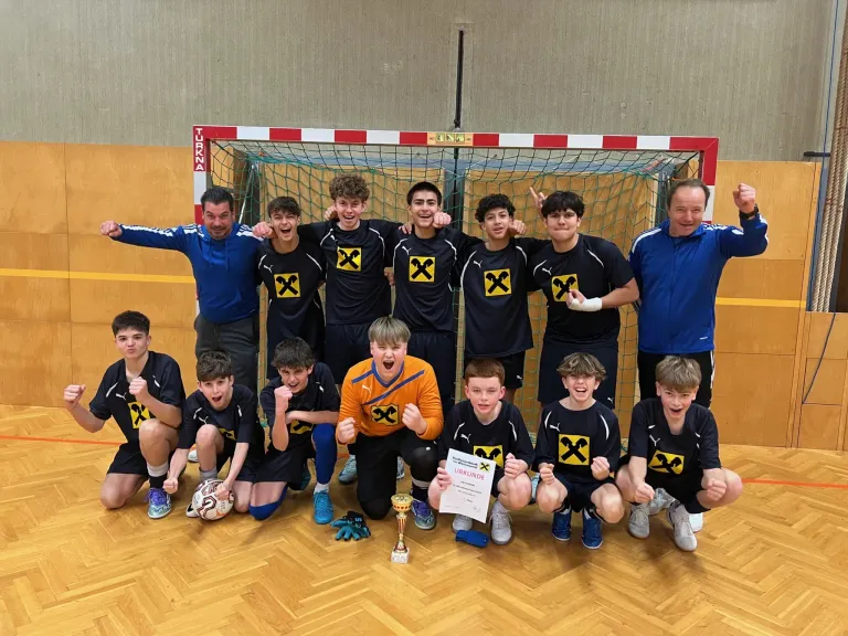 Eine Sportmannschaft in schwarzen Trikots mit gelben Kreuzen und einem orangefarbenen Trikot mit gelben Kreuzen posiert für ein Foto mit einem Pokal und einem Zertifikat.