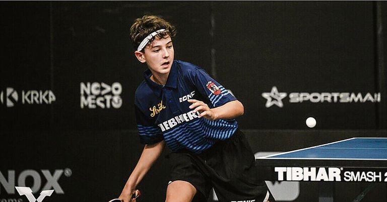 Ein junger Mann in einem blau-schwarzen Trikot mit dem Wort Stirk darauf spielt Tischtennis, sein Schläger bereit, einen Ball zu treffen.