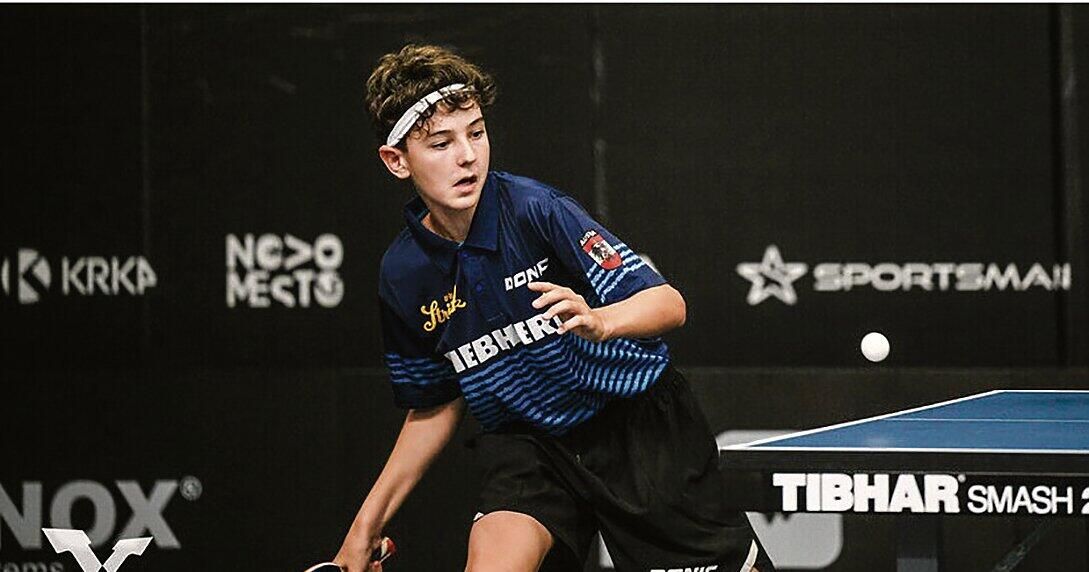 Ein junger Mann in einem blau-schwarzen Trikot mit dem Wort Stirk darauf spielt Tischtennis, sein Schläger bereit, einen Ball zu treffen.