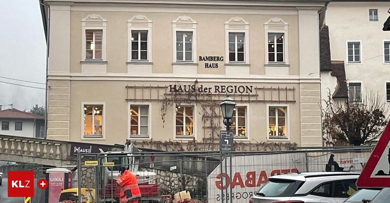 Ein Gebäude mit mehreren Fenstern und einem Schild mit der Aufschrift Bamberg Haus befindet sich im Bau. Ein Arbeiter in einer orangefarbenen Weste steht in der Nähe eines Fahrzeugs. Ein Schild mit rotem Text und dem Wort "SAUNA" ist sichtbar.