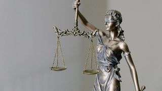 Eine bronzene Statue einer verschleierten Frau, die eine Waage in beiden Händen hält. Sie ist in ein fließendes Kleid gekleidet.