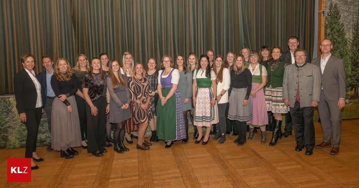 Eine Gruppe von Frauen und einem Mann posiert für ein Foto vor einem Vorhang, einige in traditioneller Kleidung, stehen auf einem Holzboden.