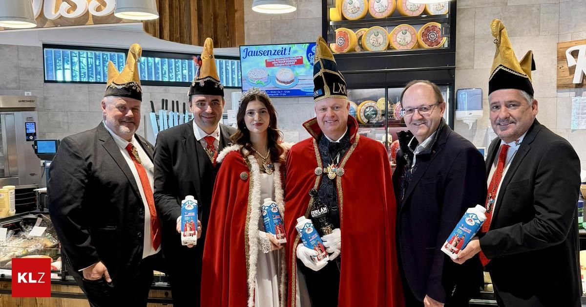 Fünf Personen in verschiedenen Kostümen stehen in einem Geschäft. Sie halten Milchkartons in den Händen. Ein Schild zeigt Jausenzeit. Dahinter ist eine Käseausstellung zu sehen.