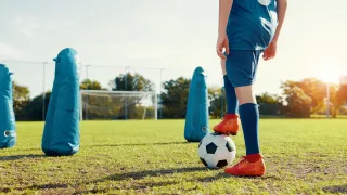 Ein Fußballspieler in blauer Uniform balanciert einen Fußball auf seinem Fuß auf einem Rasenfeld.