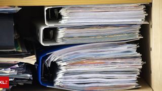 Ein Nahaufnahme von gestapelten weißen Ordnern in einem blauen Ordner, wobei zusätzliche Ordner in weißen Ordnern oben sichtbar sind.