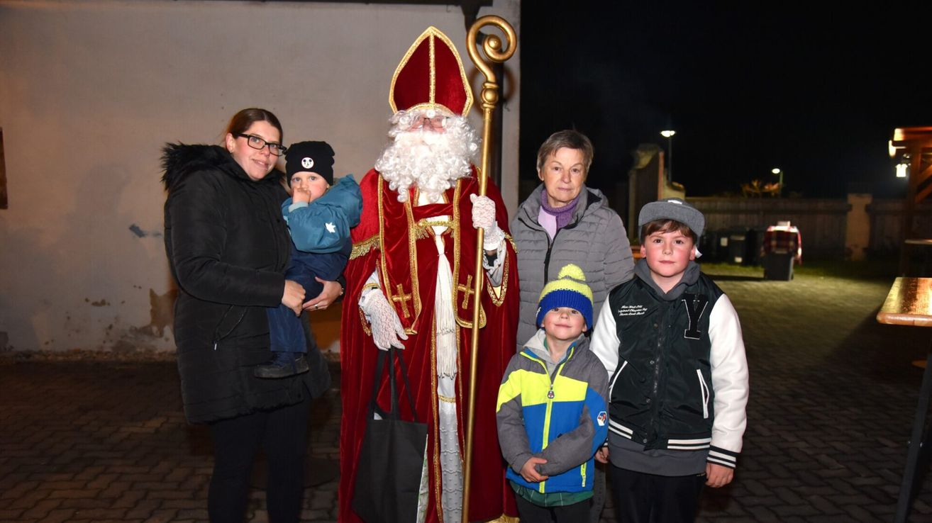 Eine Familie steht mit einer als Weihnachtsmann verkleideten Person, die ein Kind hält, und posiert für ein Foto bei Nacht.