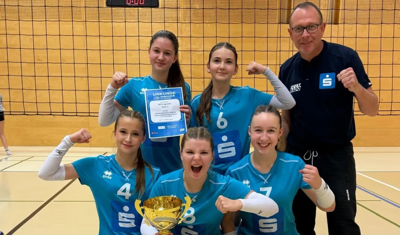 Eine Gruppe junger Frauen in blauen Trikots posiert für ein Foto mit einer Trophäe, eine hält ein Zertifikat. Ein Mann steht hinter ihnen.