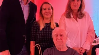 Vier Personen posieren in einem Raum mit roter und blauer Beleuchtung. Ein Mann mit Brille steht neben einer Frau mit einer Handtasche. Ein älterer Mann sitzt mit verschränkten Armen. Dahinter stehen zwei Frauen, eine mit einer Brille auf dem Kopf.