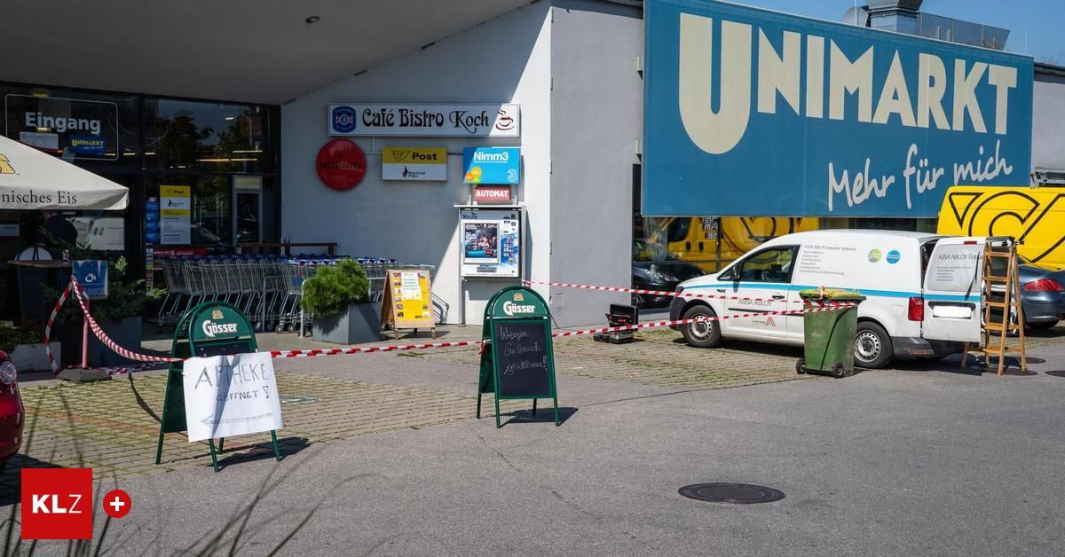 Der Eingang eines Supermarkts mit einem abgesperrten Bereich, einem geparkten weißen Lieferwagen in der Nähe und einem Schild mit Schrift darauf.