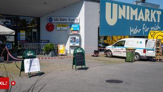 Der Eingang eines Supermarkts mit einem abgesperrten Bereich, einem geparkten weißen Lieferwagen in der Nähe und einem Schild mit Schrift darauf.