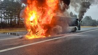 Ein Bus steht am Straßenrand in Flammen, wobei die Vorderseite vom Feuer verschlungen wird und Rauch aufsteigt.