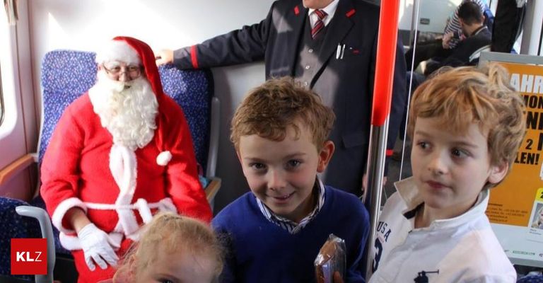 Der Weihnachtsmann in rotem Gewand steht neben einem lächelnden Jungen in einem Bus, der Schaffner steht hinter ihnen.