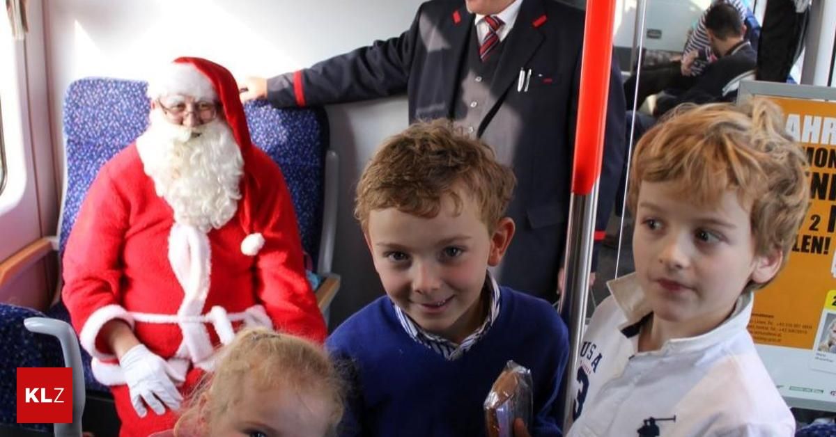 Der Weihnachtsmann in rotem Gewand steht neben einem lächelnden Jungen in einem Bus, der Schaffner steht hinter ihnen.