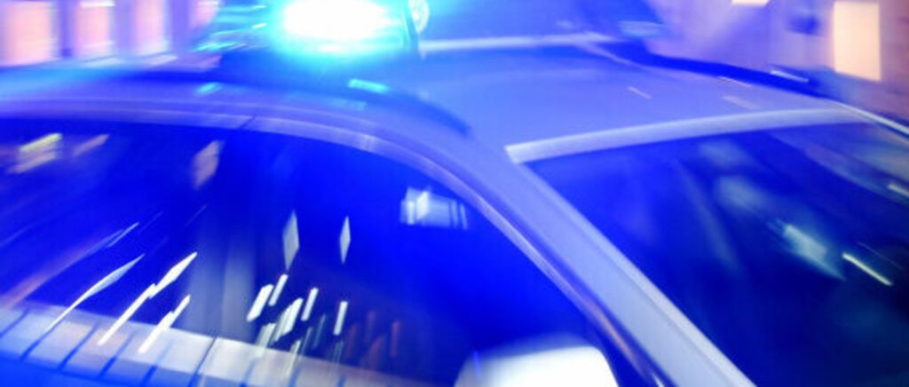 Ein Polizeiauto mit eingeschaltetem Licht ist geparkt, wobei die Fahrertür geöffnet ist.