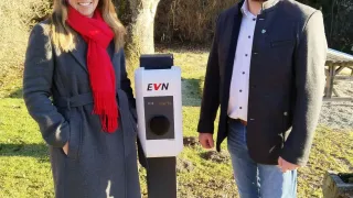Eine Frau in einem grauen Mantel und ein Mann in einem schwarzen Mantel und Jeans stehen neben einer weißen EVN-Ladestation.