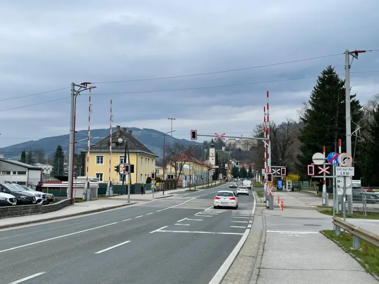 Eine leere Straße mit fahrenden Autos, gelben Gebäuden, Bergen im Hintergrund und Straßenlaternen auf beiden Seiten.