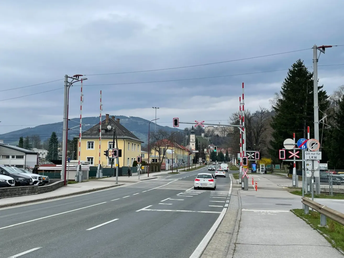 Eine leere Straße mit fahrenden Autos, gelben Gebäuden, Bergen im Hintergrund und Straßenlaternen auf beiden Seiten.