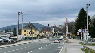 Eine leere Straße mit fahrenden Autos, gelben Gebäuden, Bergen im Hintergrund und Straßenlaternen auf beiden Seiten.